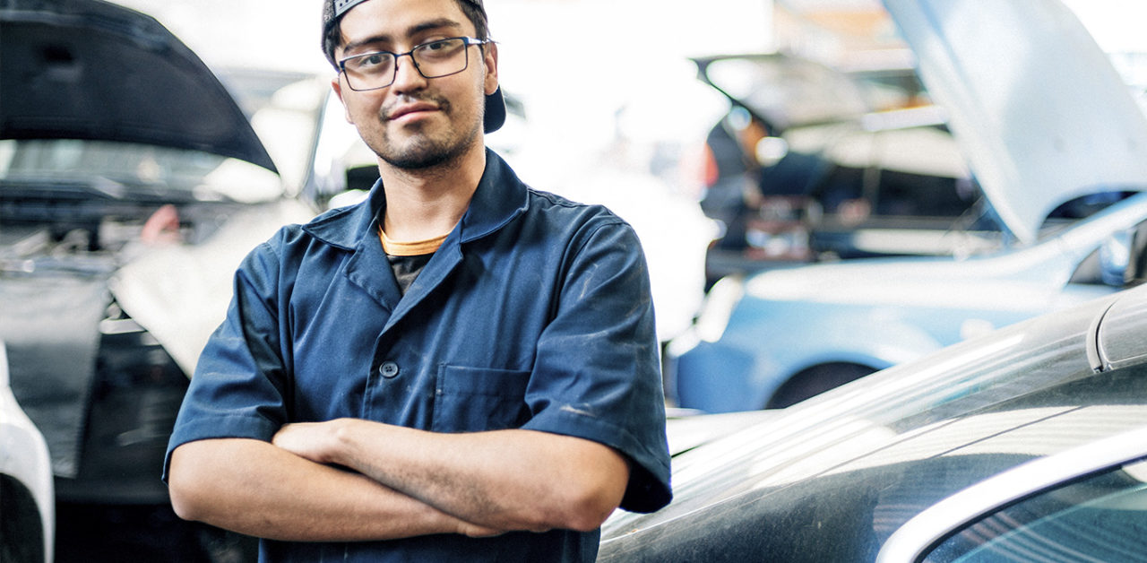 Latino mechanic standing in blue jumpsuit with arms crossed