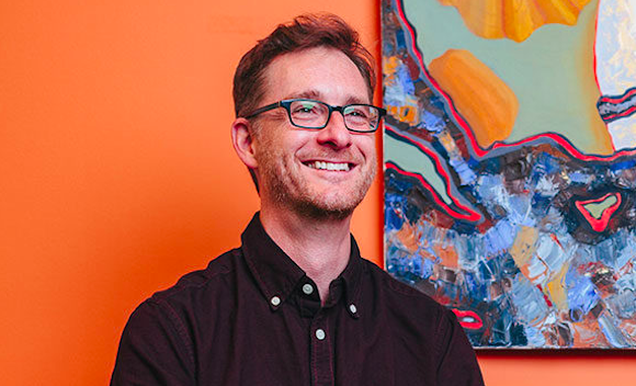 Man smiling in front of orange wall and abstract painting